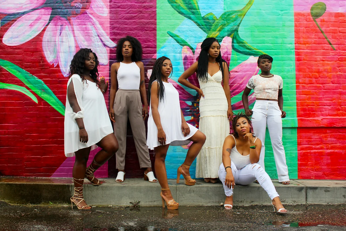 A group of Black women standing and sitting together in front of a bright floral mural