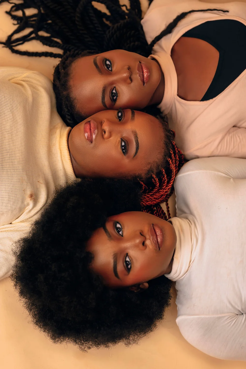 Three women lying with their heads together, looking up at the camera