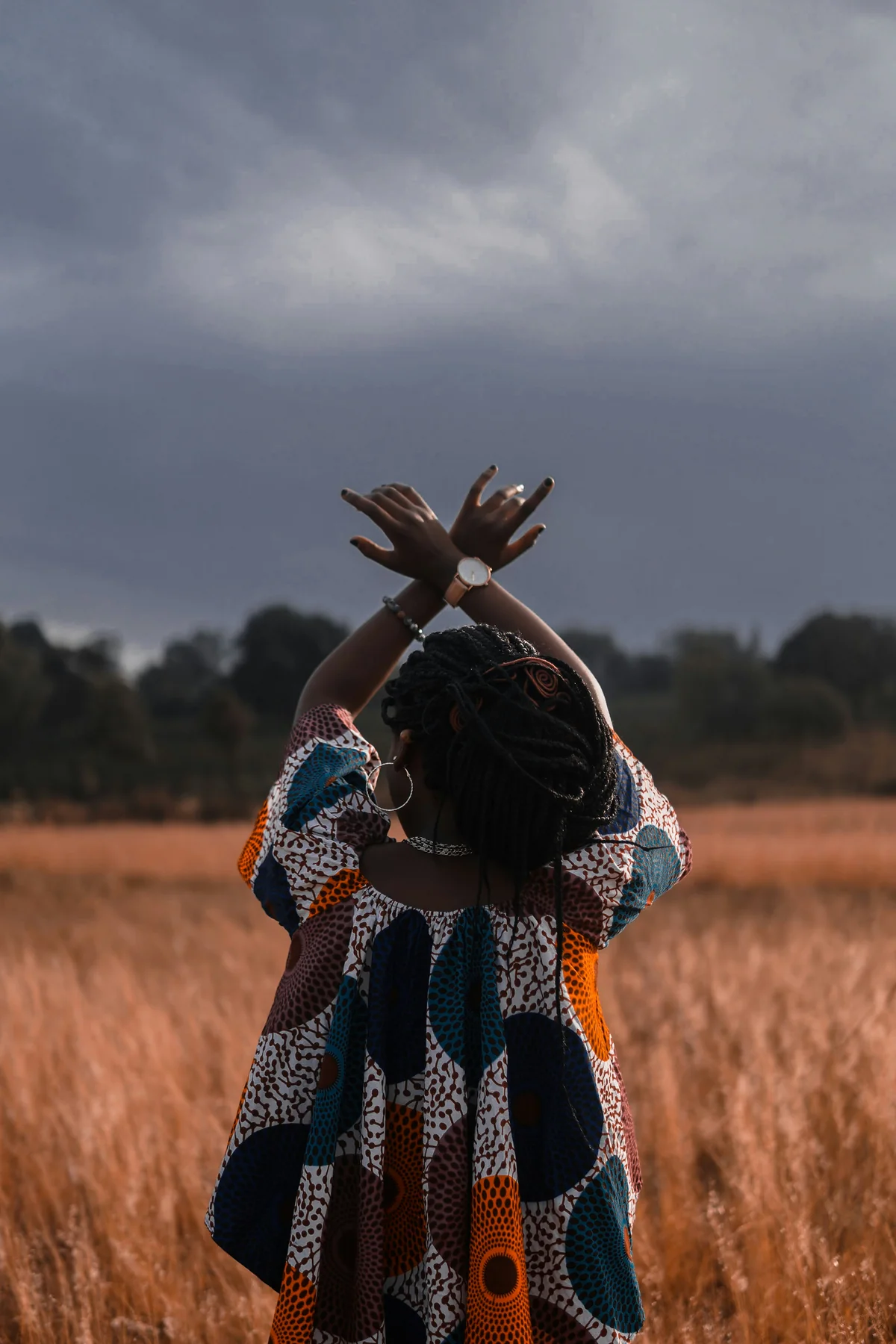 A woman in a patterned dress standing in a golden field with her arms raised overhead
